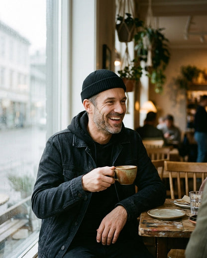 Mann i svart fisherman-lue og dongerijakke på en kafé